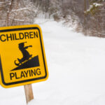 A bright yellow signsticks out of the snow. It has a graphic of a child on a sled and says "Children Playing."