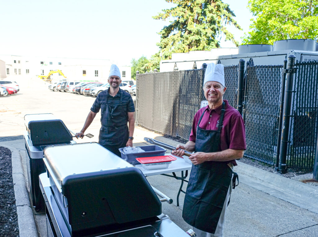 Luke Fischer and David Unmacht grill side-by-side at a summer cookout at the League of Minnesota Cities. 