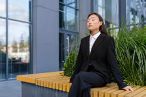 Business woman sitting on a bench relaxing and performing breathing exercises.