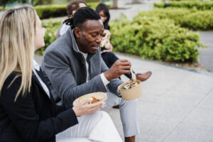 Two coworkers in business attire eating lunch outdoors.