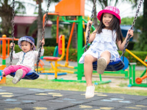 Two young girls playing on swings at a playground.