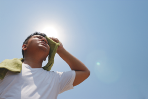 Person is shown wiping sweat from their forehead during a sunny day.