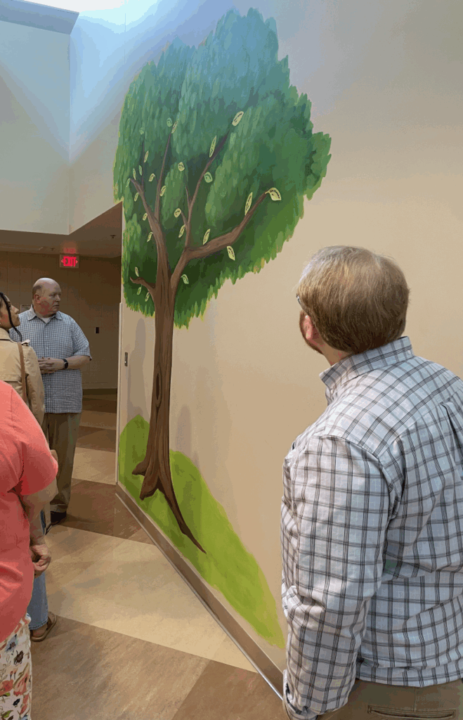 LMC and LMCIT staff members are shown admiring a mural of a tree painted on a wall within the Dakota 911 building.