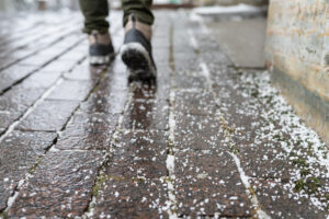 Selective focus on technical salt grains on icy sidewalk surface in wintertime, used for melting ice and snow. Applying salt to keep roads clear and people safe in winter weather from ice or snow