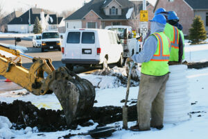 Water main workers excavate a snow-filled yard