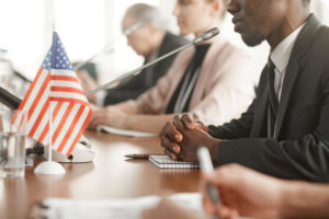 People in dress clothes sitting around a table with microphones and a small American flag.