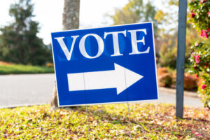 A Blue 'Vote' Sign with an Arrow on a Sunny Day, Pointing the Way to a Polling Station.